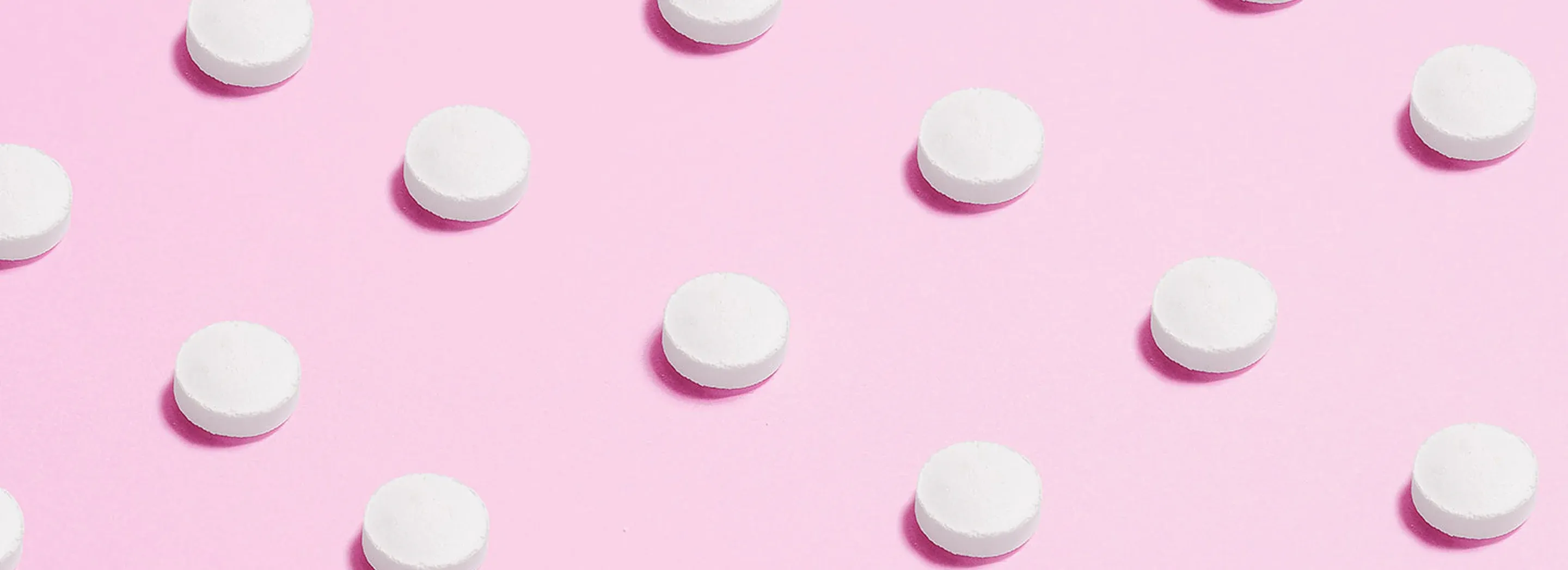 Białe tabletki ułożone w r&oacute;wnych odstępach na r&oacute;żowym tle