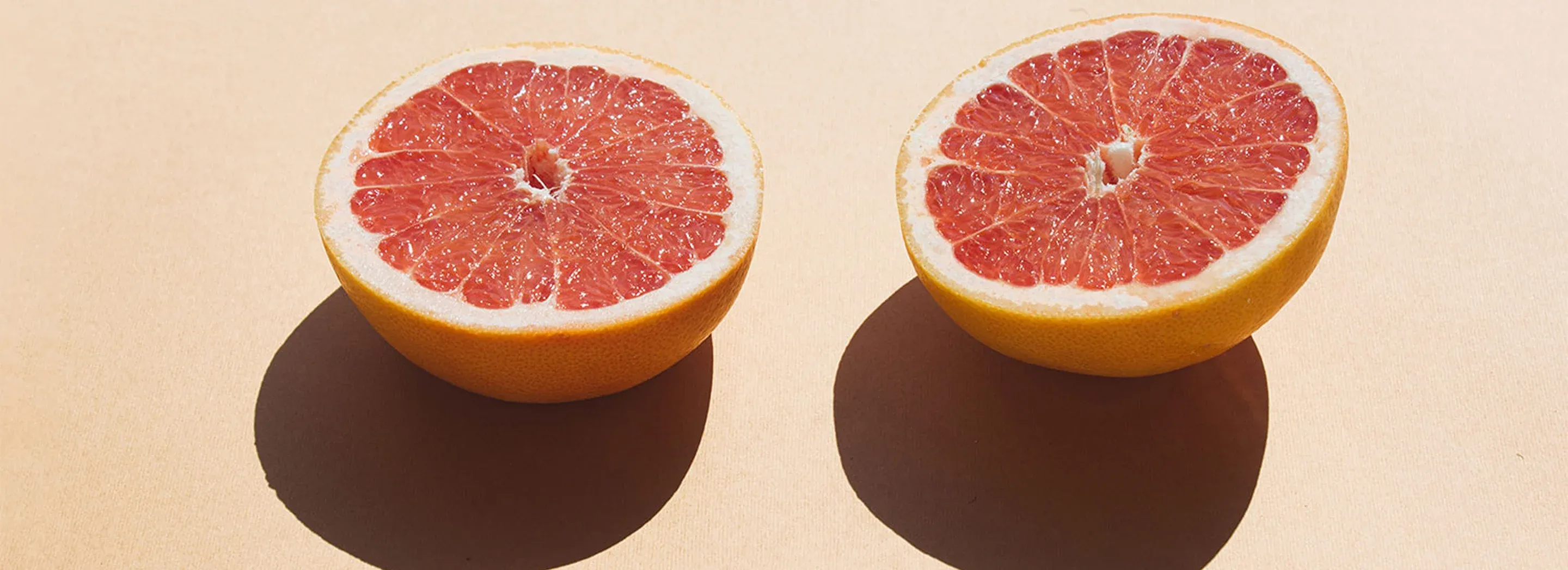 Dwie poł&oacute;wki czerwonego grejpfruta ułożone na jasnym tle &ndash; świeży owoc w naturalnym świetle