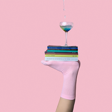 Stos książek z kieliszkiem na g&oacute;rze, na tle r&oacute;żowej ściany.