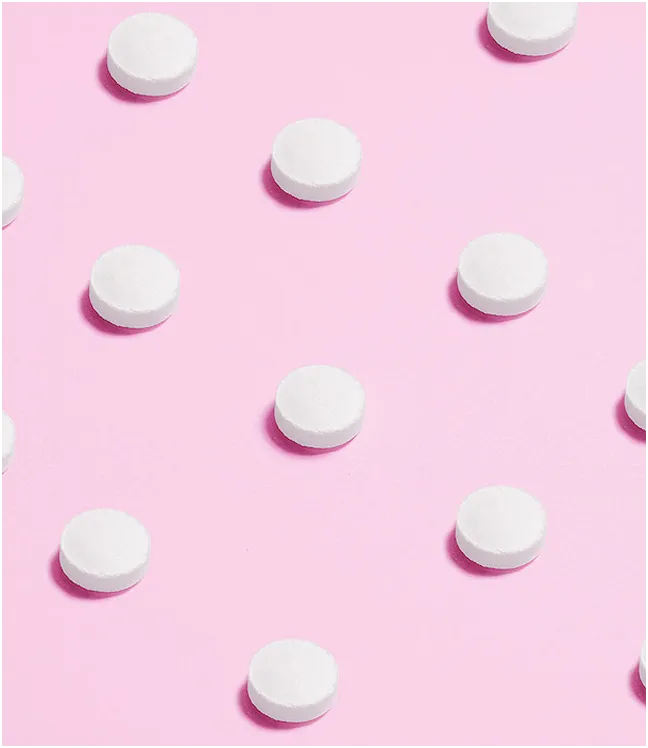 Białe tabletki ułożone w r&oacute;wnych odstępach na r&oacute;żowym tle